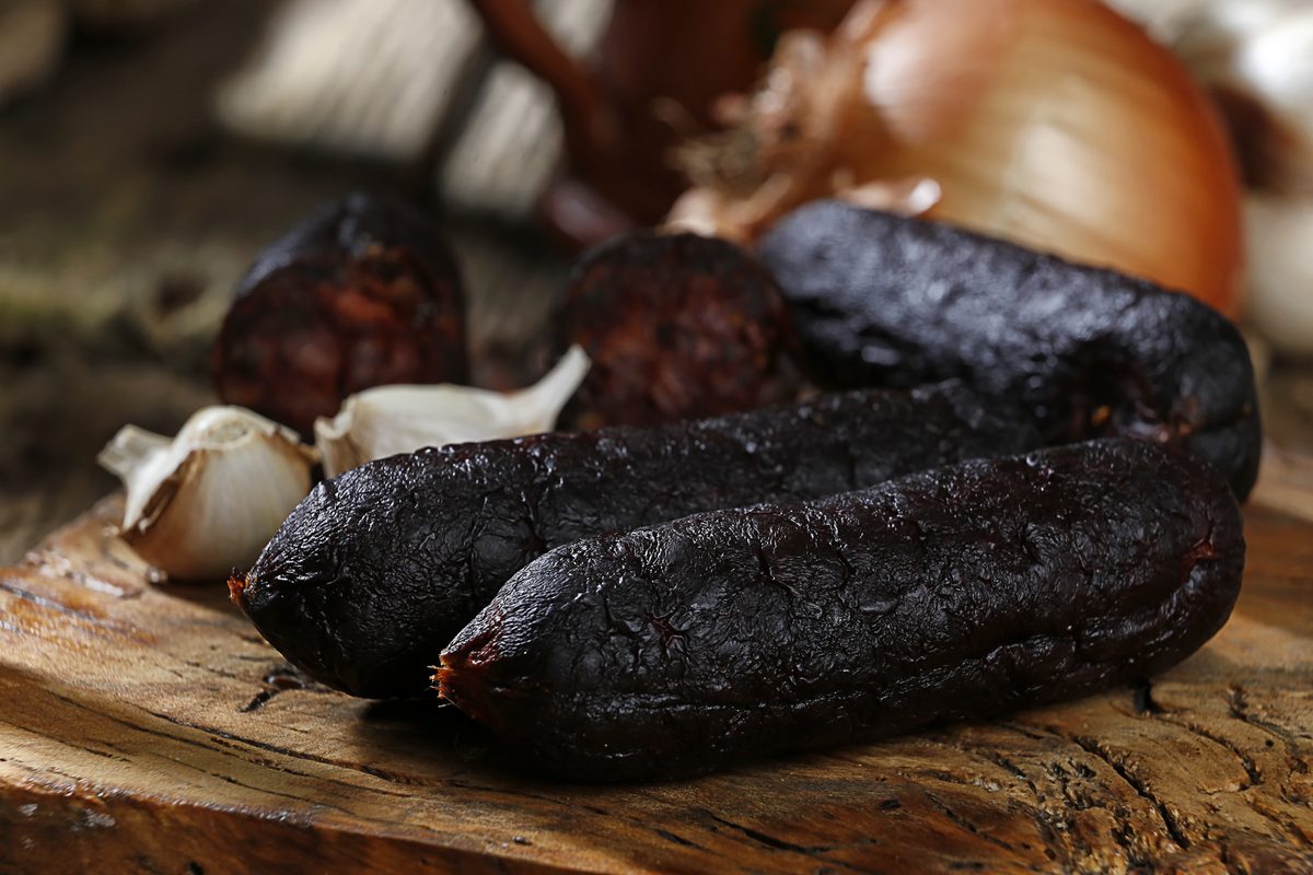 Morcilla asturiana ahumada sobre tabla de madera junto a cebolla y ajo